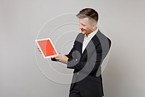 Young business man in classic black suit holding and looking on tablet pc computer with blank empty screen isolated on