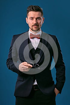 Young business man in classic black suit, white shirt and red bow-tie. Posing against a blue studio background. Mock up