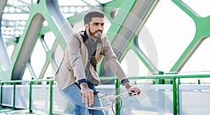 Young business man commuter with bicycle going to work outdoors in city, riding on bridge.