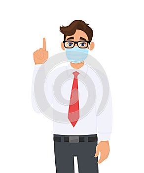 Young business man covering face with medical mask and pointing finger up symbol. Trendy person wearing facial hygienic surgical