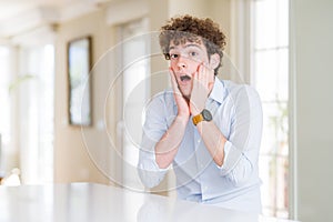 Young business man with curly read head afraid and shocked, surprise and amazed expression with hands on face