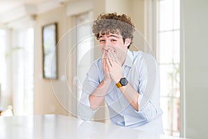 Young business man with curly read head laughing and embarrassed giggle covering mouth with hands, gossip and scandal concept