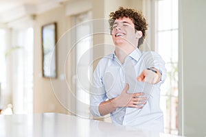 Young business man with curly read head laughing at you, pointing finger to the camera with hand over body, shame expression