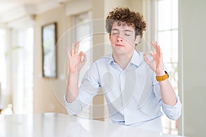 Young business man with curly read head relaxed and smiling with eyes closed doing meditation gesture with fingers