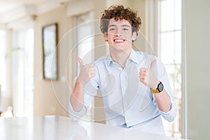 Young business man with curly read head success sign doing positive gesture with hand, thumbs up smiling and happy