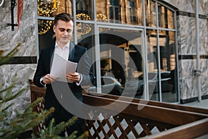 Young business man with documents and mobile phone near of modern building.