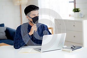 Young business man in face mask planning and working from home on laptop computer on desk for protection for outbreak.
