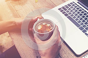 Young business man hand holding cup coffee and using laptop comp
