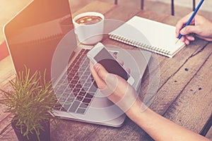 Young business man hand holding phone and using laptop computer