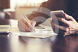 Young business man hand writing paper and hand holding phone in