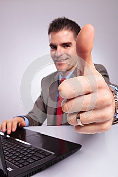 Young business man at laptop shows thumb up