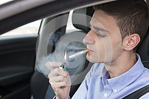 Young business man lighting cigarette inside car