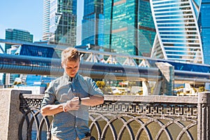 A young business man looks at his watch by the glass skyscrapers