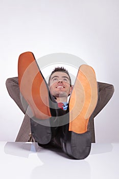 Young business man looks up with hands behind head and feet on d