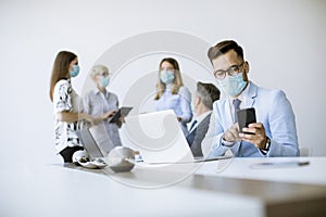 Young business man with medical protective mask works on a laptop and using mobile phone