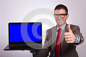 Young business man presents laptop with thumb up