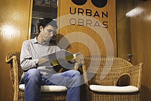 A young business man reading an architectural book in front of the office door before a meeting with his colleagues and coworkers