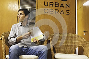 A young business man reading an architectural book in front of the office door before a meeting with his colleagues and coworkers