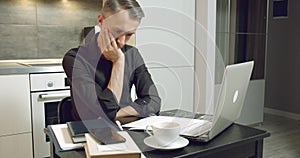 Young business man reading a contract or report and drinking coffee while working on laptop at home