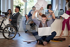 Young business man receiving a good news on his laptop. Throwing papers from happines. Casual business concept