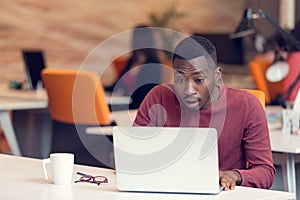 Young business man with a shocked expression working on a laptop