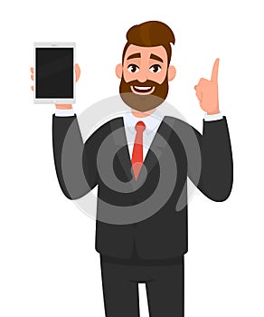 Young business man showing/holding blank screen of new digital tablet computer and pointing index finger up. Modern technology.