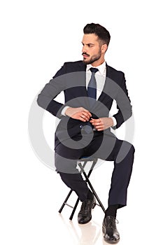 Young business man sitting on chair and buttoning his suit