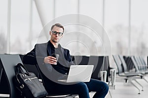 Young business man sitting on the computer at the airport waiting for the flight