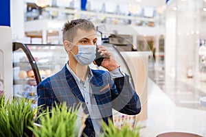 Young business man sitting in a mask in a cafe talking on the phone