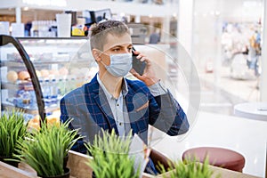 Young business man sitting in a mask in a cafe talking on the phone