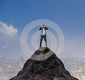 Young business man standing on top of mountain and spying by bin