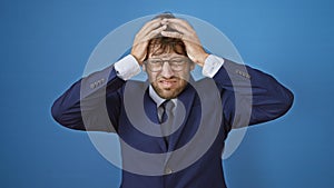 Young business man stressed with severe headache, clutching his head in pain. isolated on blue background, bearing an expression