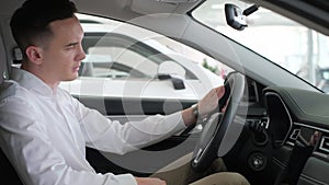 Young business man stroking the steering wheel in an electric car. Buying a new car at a dealership