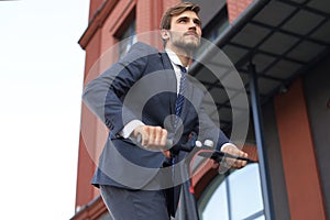 Young business man in suit riding on electric scooter on a business meeting. Ecologic transport concept.