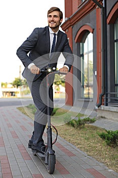 Young business man in suit riding on electric scooter on a business meeting. Ecologic transport concept.