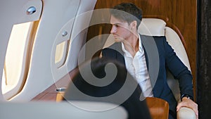 Young business man in suit sitting in first class airplane. Respectable rich man in suit flying in in private jet plane.