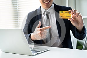 Young business man in a suit with a smile and pointing his finger at the yellow credit card.