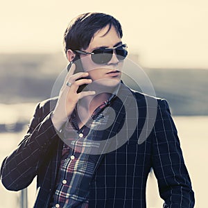 Young business man in sunglasses using smart phone on city street
