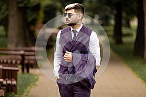Young business man in sunglasses and wearing on violet luxery three-piece suit looks to side while walking on street