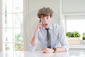Young business man talking on smartphone at the office scared in shock with a surprise face, afraid and excited with fear