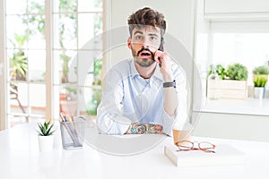 Young business man talking on smartphone scared in shock with a surprise face, afraid and excited with fear expression