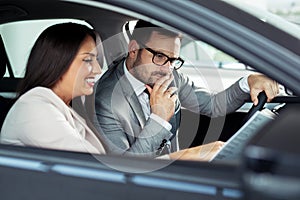 Young business man test dAttractive saleswoman showing inside of a car to customer	rive new car