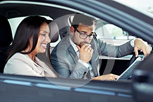 Young business man test dAttractive saleswoman showing inside of a car to customer	rive new car