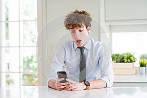 Young business man using smartphone at the office scared in shock with a surprise face, afraid and excited with fear expression