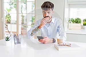 Young business man using smartphone sending a message cover mouth with hand shocked with shame for mistake, expression of fear,