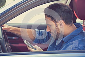 Young business man using texting on mobile phone while driving a car