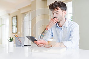 Young business man using touchpad tablet cover mouth with hand shocked with shame for mistake, expression of fear, scared in