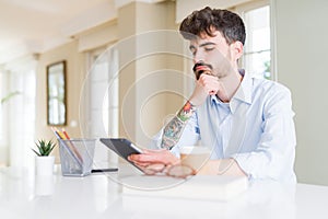 Young business man using touchpad tablet serious face thinking about question, very confused idea