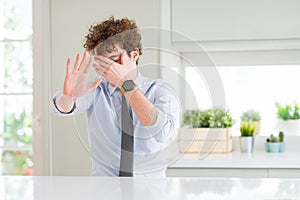 Young business man wearing a tie covering eyes with hands and doing stop gesture with sad and fear expression