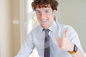 Young business man wearing a tie doing happy thumbs up gesture with hand